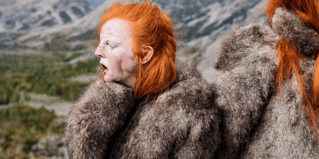 Close-up shot ginger woman, sad, talking, open mouth, worn leather, fur, walking on a hiking trail in the mountains, battleworn suit , wearing tight winter clothing, walking on a hiking trail in the mountains, angry, hair as messy ponytail, most realistic skin texture, picture taken with canon eos 3
